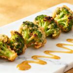 Crispy air fryer broccoli tempura with a light golden coating served on a platter with dipping sauce