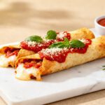 Crispy air fryer pizza taquitos filled with melted cheese and topped with marinara sauce and basil