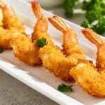 Crispy air fryer butterfly shrimp with a golden crunchy coating served with lemon wedges and fresh herbs