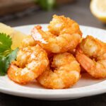 Asian air fryer shrimp with a crispy golden coating served with lemon wedges and fresh herbs