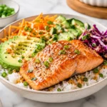 Salmon rice bowl with avocado, cucumber, shredded carrots, purple cabbage, and white rice