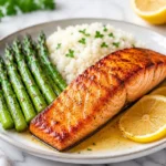 Grilled salmon fillet served with asparagus, white rice, and lemon slices on a plate