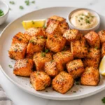 Plate of crispy air fryer salmon bites with lemon wedges and creamy dipping sauce on a marble kitchen counter