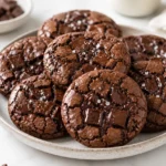 Fudgy air fryer double chocolate cookies stacked on a ceramic plate with melted chocolate chunks, crackled tops, and flaky sea salt on a bright marble countertop.
