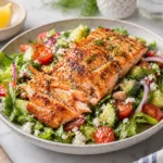 Air fryer salmon salad with grilled salmon fillets, cucumbers, cherry tomatoes, red onions, feta cheese, and fresh greens served on a ceramic plate.