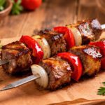 Air Fryer Beef Kabobs with juicy grilled beef cubes, red bell peppers, and onions on metal skewers served on a wooden board