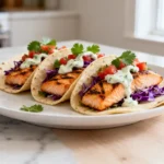 Grilled salmon tacos with purple cabbage, pico de gallo, and creamy cilantro sauce on soft tortillas