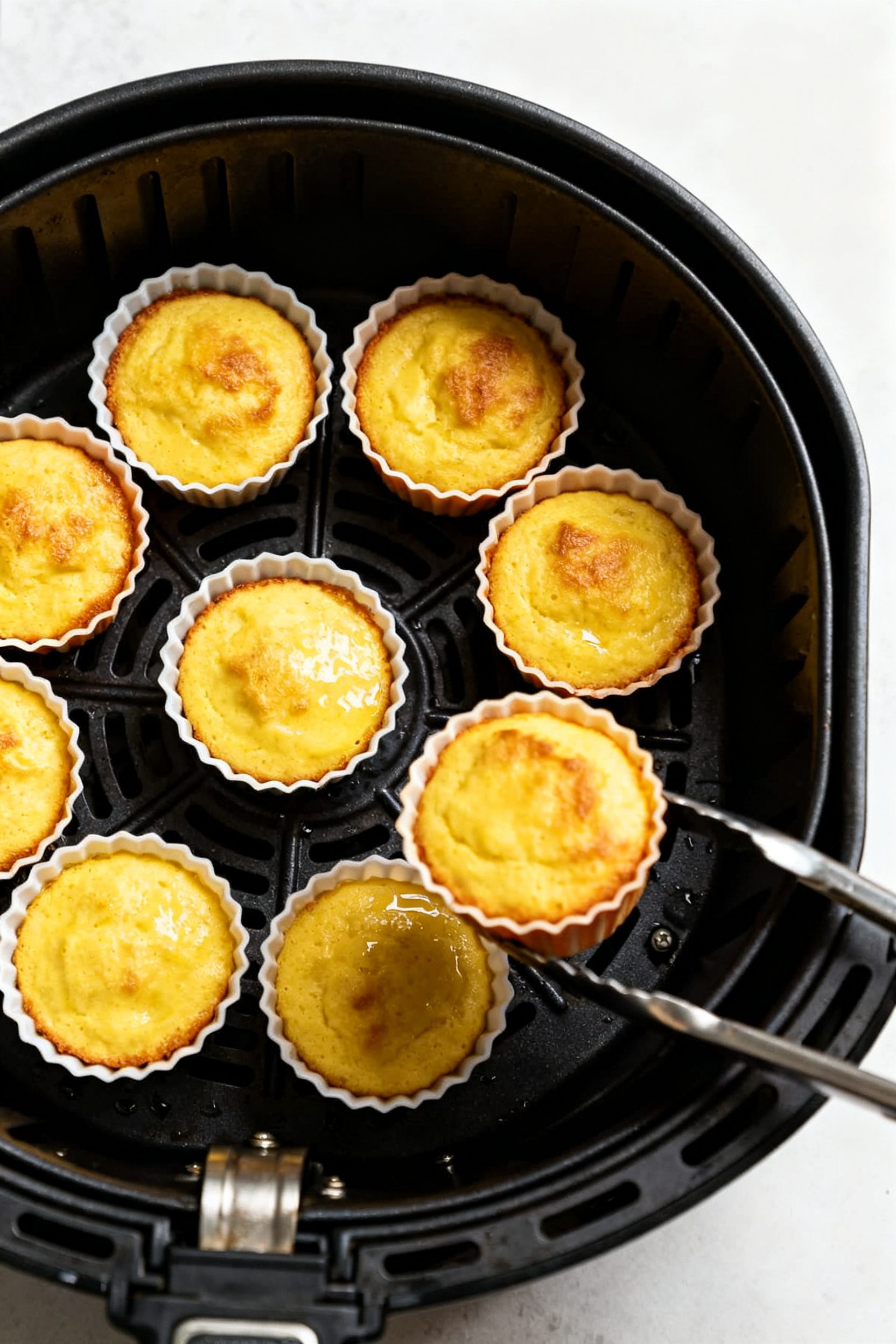 Cooking process: Overhead shot of muffin batter-filled silicone cups spaced in an air fryer basket m
