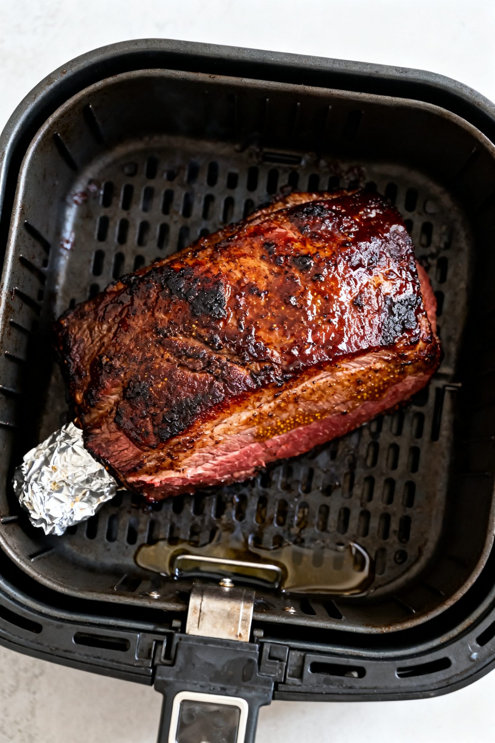 Cooking process: Unwrapped, fully cooked corned beef brisket in the air fryer basket during the “b