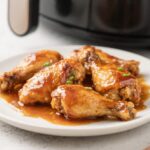 Crispy honey glazed chicken cooked in the air fryer with a sweet sticky glaze on a white plate