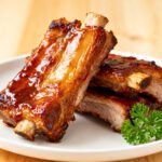 Air fryer barbecue pork ribs glazed with smoky sauce and served with pickles, coleslaw, and extra barbecue sauce