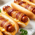 Air fryer bacon wrapped hot dogs topped with melted cheese and wrapped in crispy smoky bacon