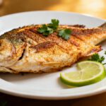 Whole air fryer tilapia with crispy golden skin, tender flaky flesh, and fresh lime wedges