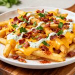 Air fryer bacon cheese fries topped with crispy bacon, melted cheddar cheese, creamy sauce, and golden fries