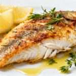 Air fryer baked tilapia with tender flaky fish, golden seasoned crust, fresh herbs, and lemon wedges