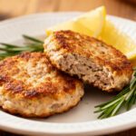 Juicy air fryer turkey patties with a golden brown crust, served on a white plate with fresh rosemary sprigs and lemon wedges.