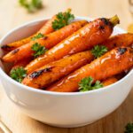 Air fryer hot honey carrots glazed with sweet and spicy honey sauce, roasted until caramelized and served in a white bowl with fresh parsley garnish.