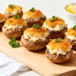 Air fryer crab stuffed mushrooms topped with golden crispy breadcrumbs, arranged on a wooden serving board and garnished with fresh parsley.