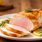 Juicy air fryer turkey breast with a golden roasted exterior, sliced and served on a white plate with fresh rosemary sprigs and lemon slices.