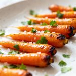 Air fryer baby carrots roasted until tender and caramelized, topped with coarse sea salt and fresh parsley on a serving platter.
