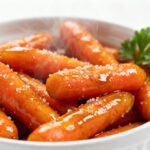Air fryer glazed carrots coated in a sweet buttery glaze, roasted until tender and caramelized, served in a white bowl with fresh parsley.