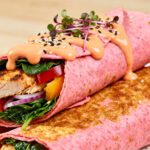Air fryer pink protein wraps filled with grilled chicken, fresh spinach, red peppers, and onions, topped with creamy sauce, sesame seeds, and microgreens.