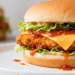 Air fryer spicy chicken sandwich with crispy breaded chicken, melted cheddar cheese, fresh lettuce, and spicy sauce on a soft toasted bun.