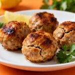 Air fryer turkey meatballs with a golden brown crust and juicy interior, served on a white plate with fresh parsley and lemon wedges.