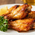 Air fryer turkey wings with crispy golden skin and juicy meat, served on a white plate with fresh parsley and lemon wedges.