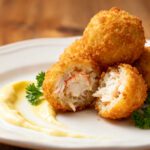 Air fryer crab balls with a crispy golden breadcrumb coating, filled with tender crab meat and served with creamy dipping sauce and fresh parsley.