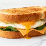 Air fryer egg sandwich with a fried egg, melted cheddar cheese, and fresh spinach on toasted bread, perfect for a quick and satisfying breakfast.