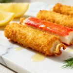 Air fryer crab sticks coated in crispy golden breadcrumbs, served with lemon wedges and fresh dill, featuring a crunchy exterior and tender seafood center.