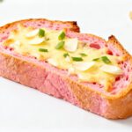 Air fryer pink garlic bread topped with melted cheese, garlic slices, and green onions on vibrant pink bread with a crispy golden crust.