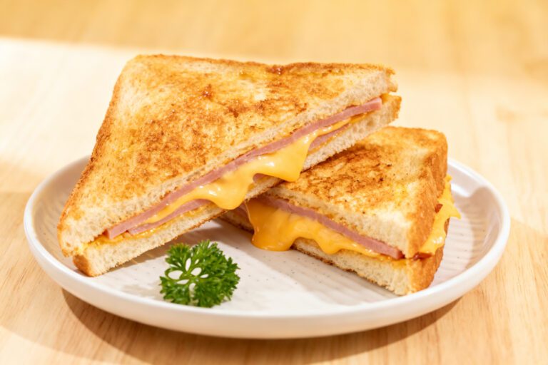 Air fryer ham and cheese sandwich with toasted golden bread, sliced ham, and melted cheddar cheese, served warm on a white plate.