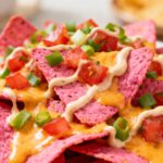 Air fryer pink nachos topped with melted cheese, diced tomatoes, green onions, and creamy sauce, featuring crispy colorful tortilla chips and bold flavor.