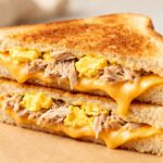 Air fryer tuna egg cheese sandwich with flaky tuna, chopped eggs, and melted cheddar cheese between crispy golden toasted bread slices.