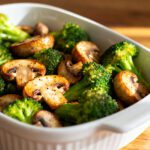 Air fryer broccoli and mushrooms roasted until tender with lightly crispy edges, served in a baking dish as a healthy and flavorful vegetable side dish.
