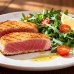 Air fryer ahi tuna steaks seared on the outside and tender in the center, served with arugula, cherry tomatoes, lemon wedges, and a light drizzle of olive oil.