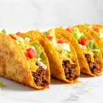 Air fryer tacos filled with seasoned ground beef, shredded lettuce, diced tomatoes, and melted cheese in crispy golden taco shells.