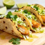Air fryer fish tacos with crispy golden fish, fresh cilantro lime slaw, and soft tortillas, served with lime wedges for a light and flavorful meal.