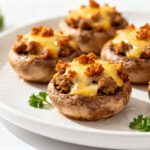 Air fryer sausage stuffed mushrooms filled with savory sausage, topped with melted cheese and crispy crumbles, served as a warm and flavorful appetizer.