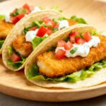 Air fryer fish tacos with crispy breaded fish fillets, fresh lettuce, diced tomatoes, and creamy sauce in soft tortillas. A light and flavorful seafood meal.