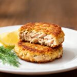 Air fryer tuna cakes with a crispy golden crust and tender flaky tuna filling, served with fresh dill and lemon wedges on a white plate.