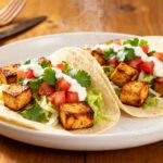 Air fryer tofu tacos with crispy seasoned tofu cubes, shredded lettuce, diced tomatoes, fresh cilantro, and creamy sauce in soft tortillas.