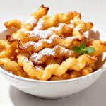 Air fryer funnel cake fries dusted with powdered sugar and served in a bowl with a crispy golden exterior and soft fluffy interior.