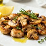 Air fryer keto mushrooms roasted until golden brown and tender, seasoned with herbs and garlic, and served with lemon wedges and fresh rosemary.