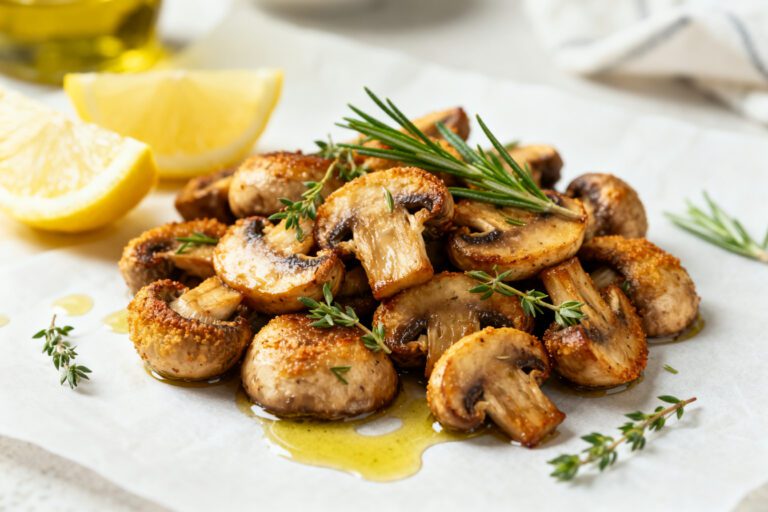 Air fryer keto mushrooms roasted until golden brown and tender, seasoned with herbs and garlic, and served with lemon wedges and fresh rosemary.