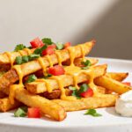 Air fryer Taco Bell nacho fries topped with creamy cheese sauce, diced tomatoes, and fresh cilantro, served with crispy seasoned fries and a side of sour cream.