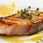 Air fryer frozen tuna steak cooked until tender and juicy, featuring a lightly seared exterior, served with lemon wedges, fresh herbs, and a buttery glaze.