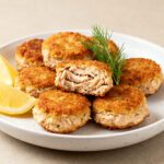 Air fryer tuna bites with a crispy golden crust and tender flaky tuna filling, served with lemon wedges and fresh dill on a white plate.